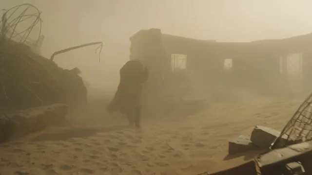 Wide-angle shot. A lone figure with a large backpack walking through a dust sto…