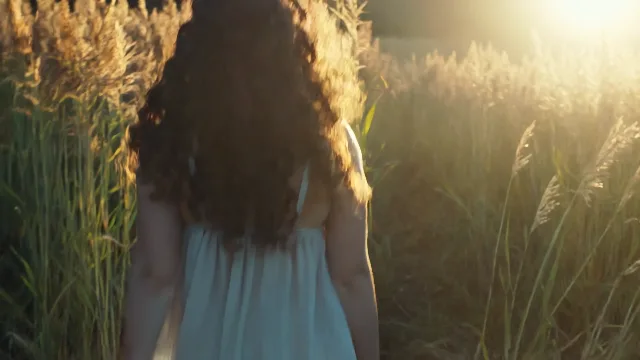 Golden hour shot. A young woman with curly hair walking in a field of tall gras…